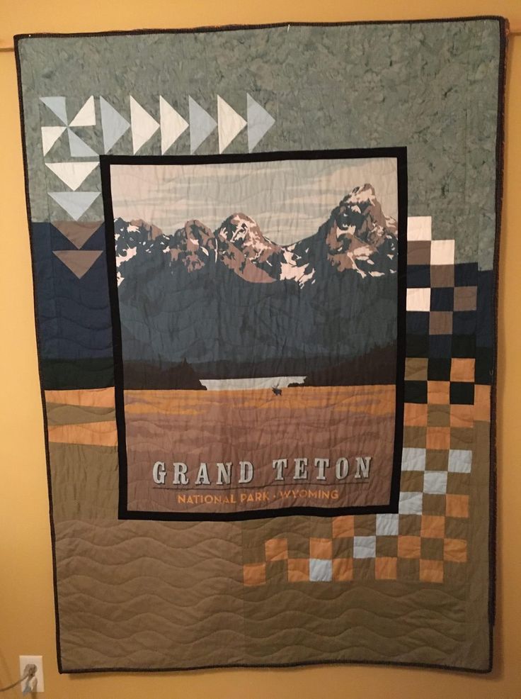 a large quilt hanging on the wall with mountains in the background and words grand titon