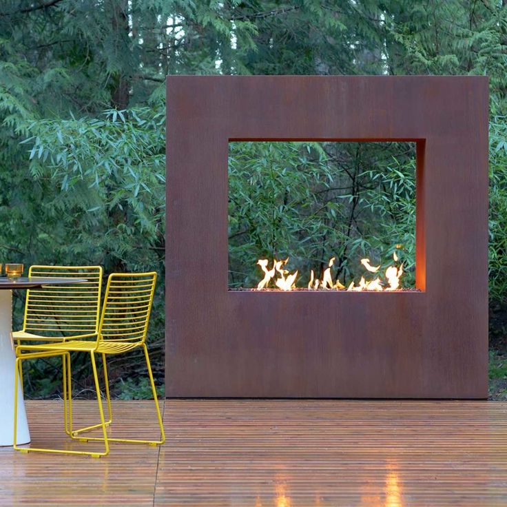 a fire pit sitting on top of a wooden deck next to two yellow chairs and a table