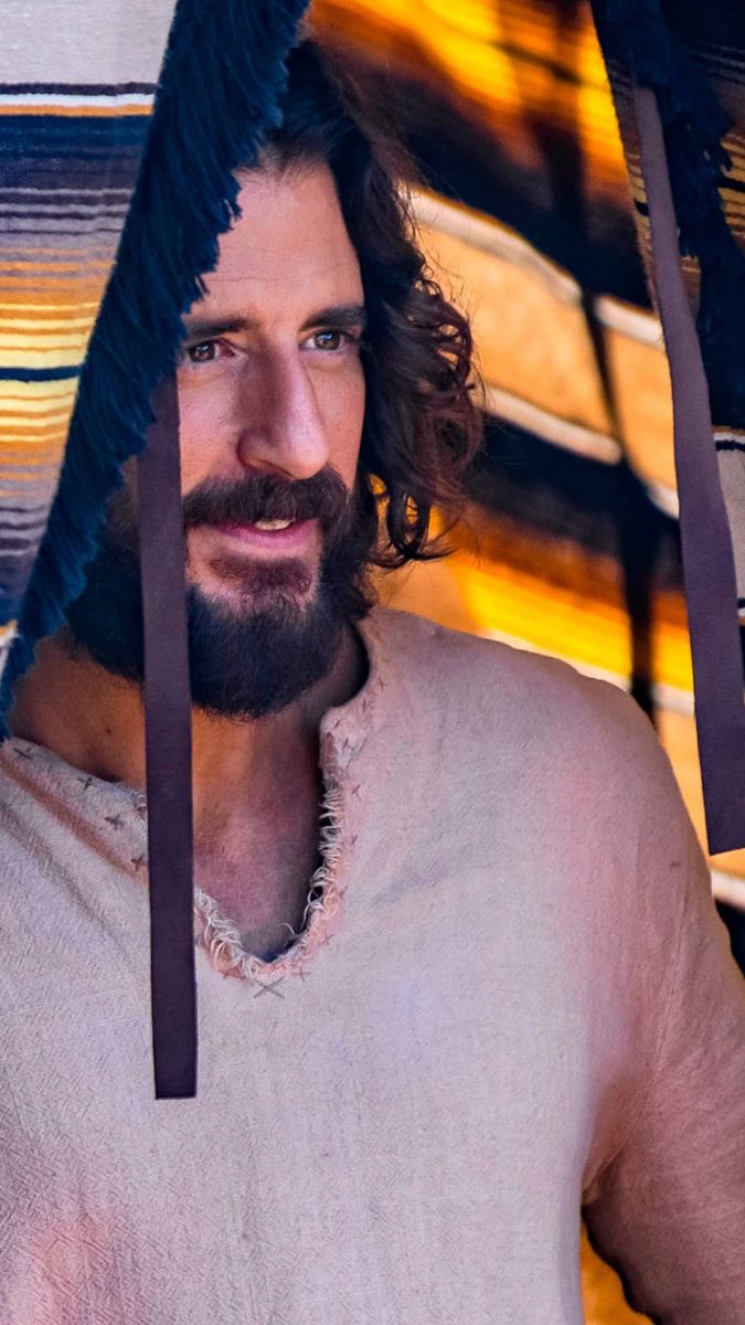 a man with long hair and beard wearing a white shirt under an umbrella that has blue fringes on it