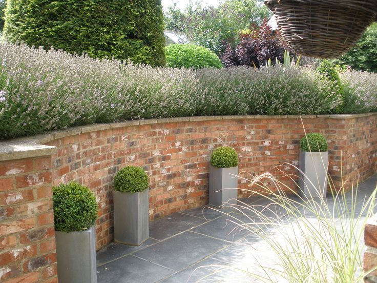 three planters are lined up against a brick wall with lavender in the foreground