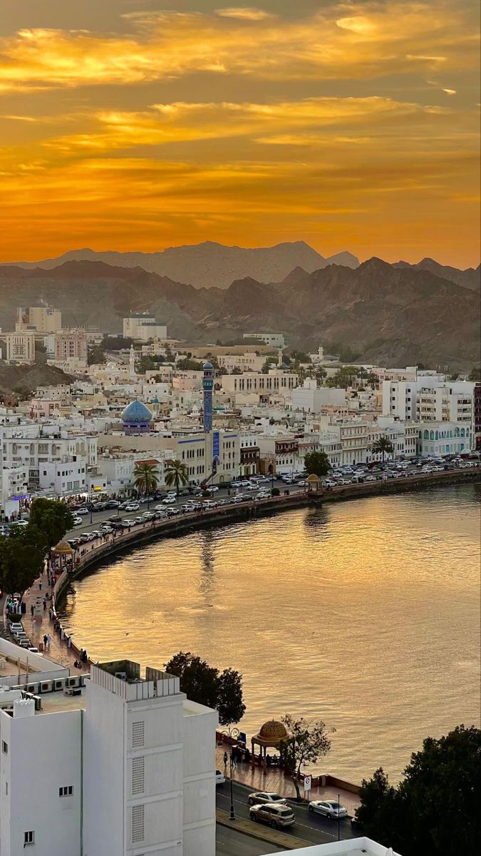 the sun is setting over a city with mountains in the background and water on the other side