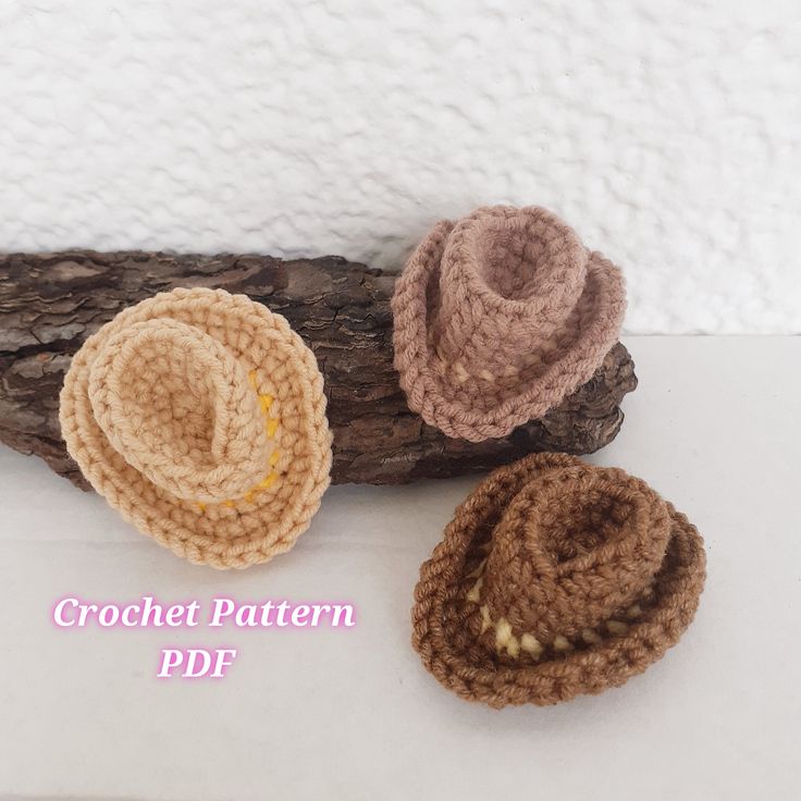 three crochet hats sitting on top of a piece of driftwood next to each other