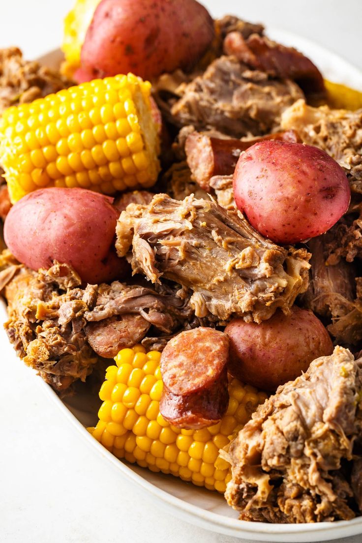 corn on the cob, potatoes and meat in a white bowl with red potatoes