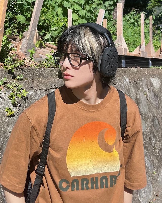 a young man wearing headphones standing in front of a rock wall