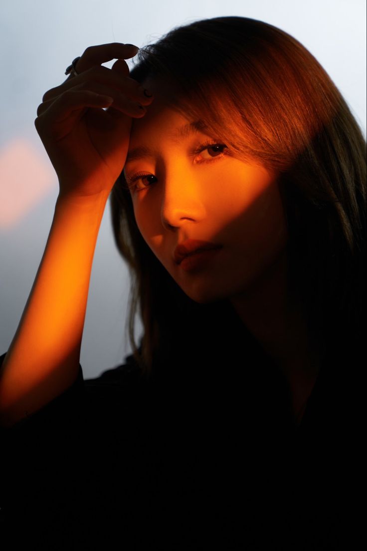 a woman is holding her head in front of the camera with an orange light shining on her face