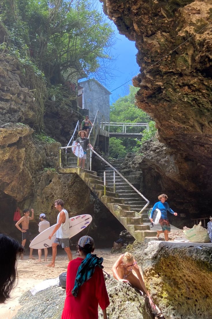 several people with surfboards are standing on the rocks and stairs leading up to a beach