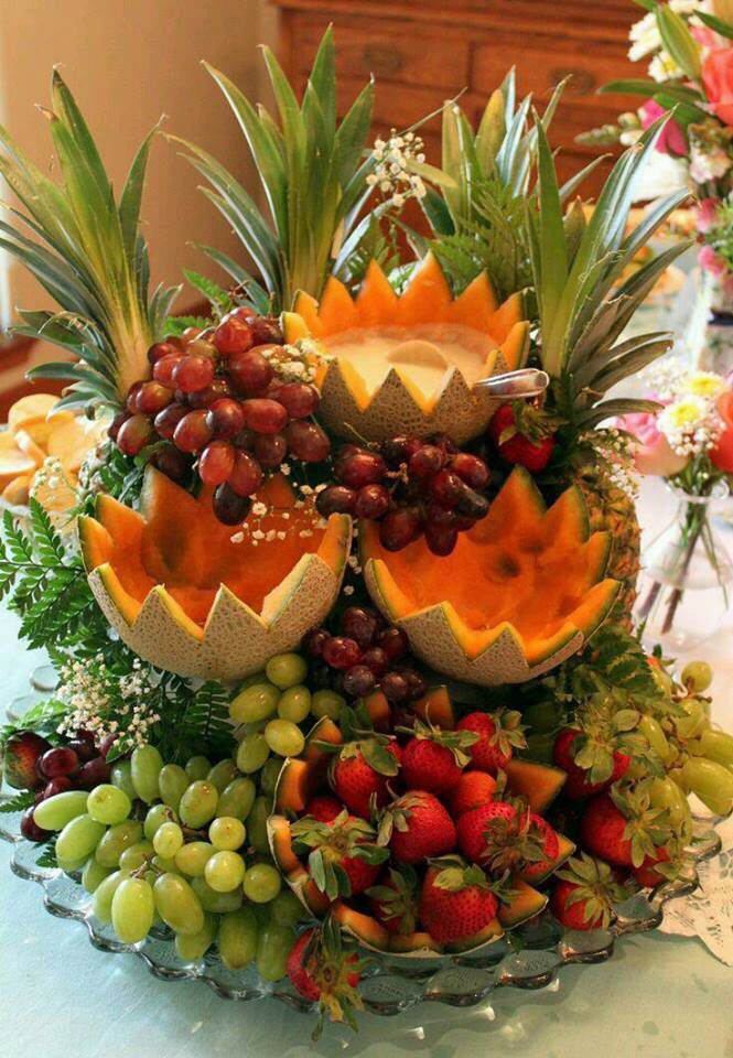 an arrangement of fruit is displayed on a table with flowers and other items in the background