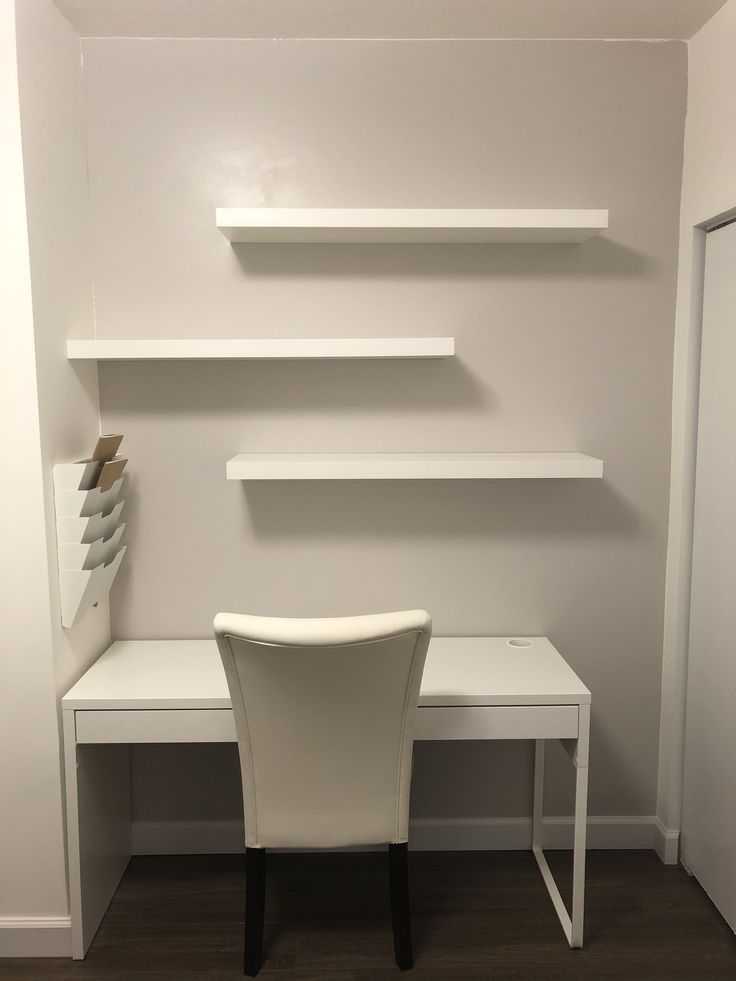 there is a white desk and chair in the room with shelves on the wall behind it