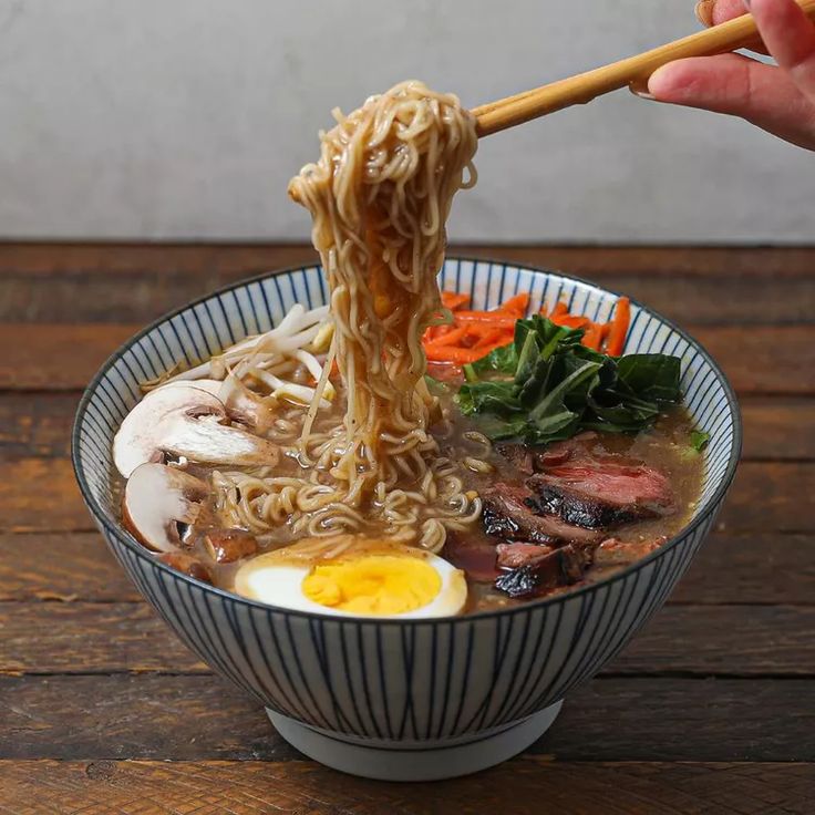 someone is holding chopsticks above a bowl of ramen with meat and vegetables