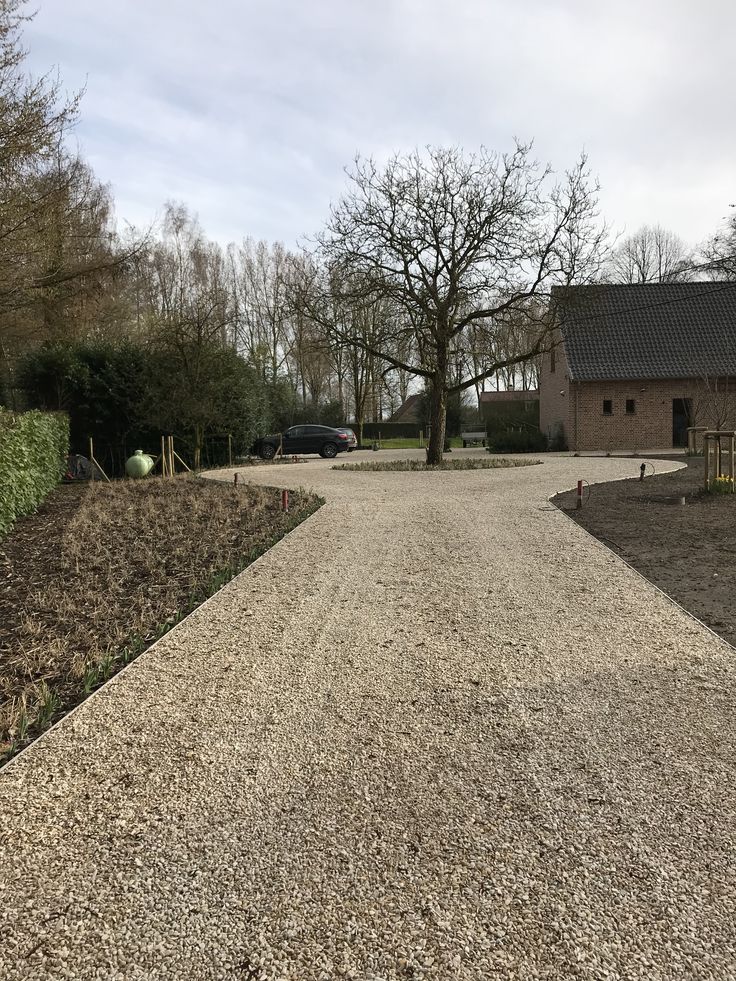 a gravel driveway leading to a house with trees in the background