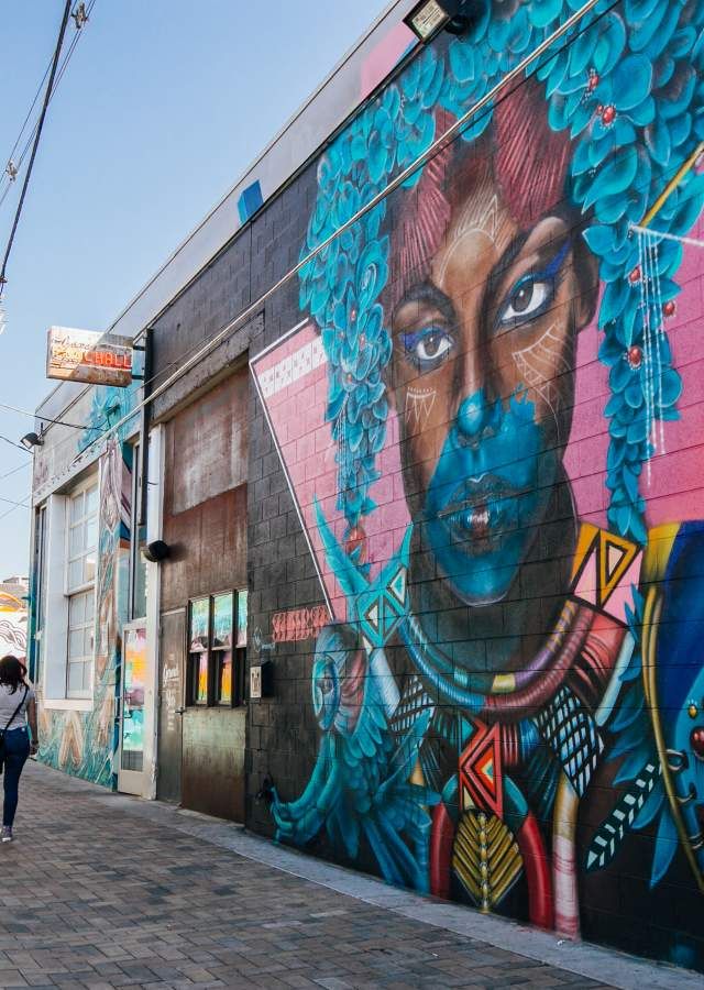 a woman walking down a sidewalk next to a wall with a painting on it's side