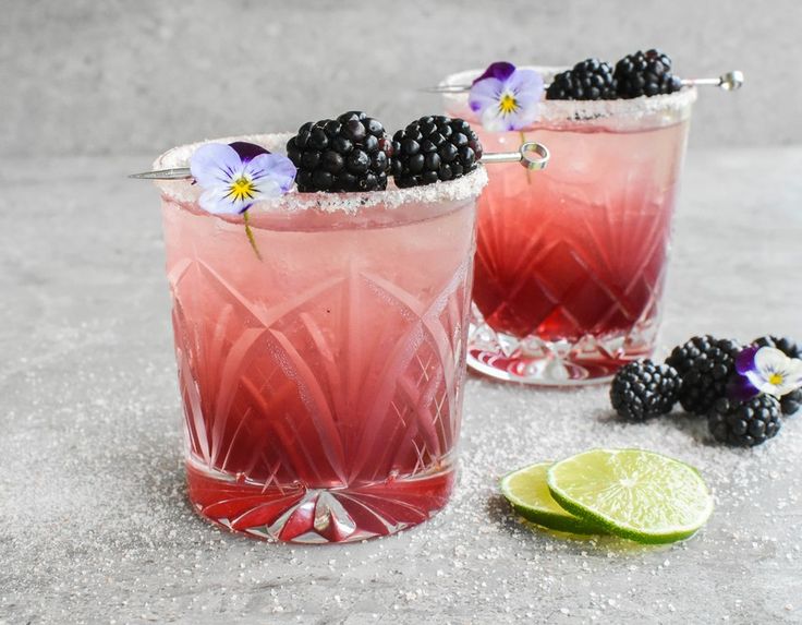 two glasses filled with raspberry lemonade and blackberries next to lime wedges