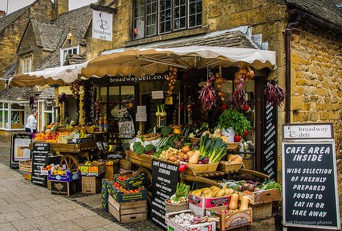 an open air market with lots of fresh produce on the side of the road in front of stone buildings