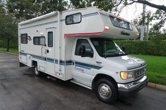 an rv is parked on the side of the road in front of some grass and trees