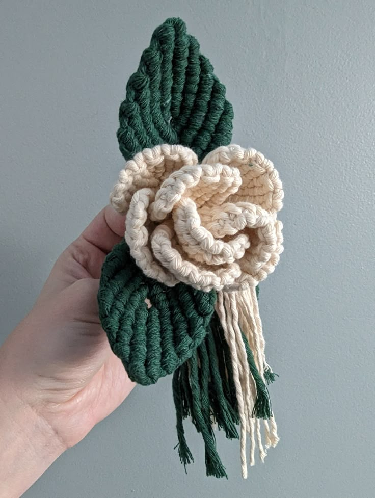 a hand holding a crocheted flower with tassels