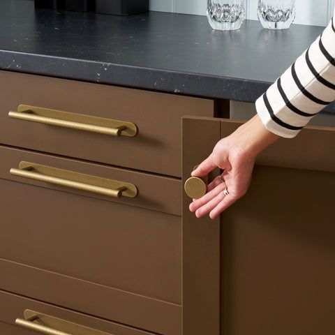 a woman's hand reaching for the drawer knobs on a kitchen countertop