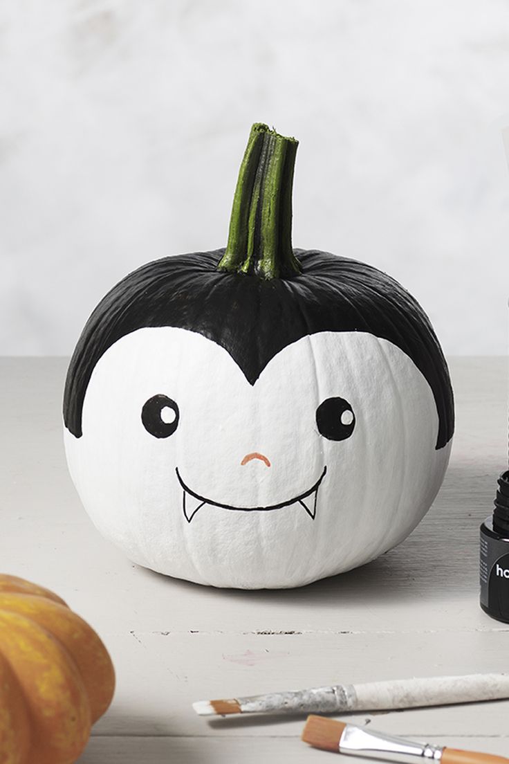 a white pumpkin decorated with black and white face painted on it, next to some paintbrushes