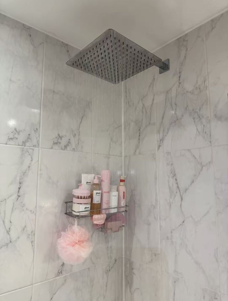 a shower head with soap and lotion on it in a white marble tiled bathroom