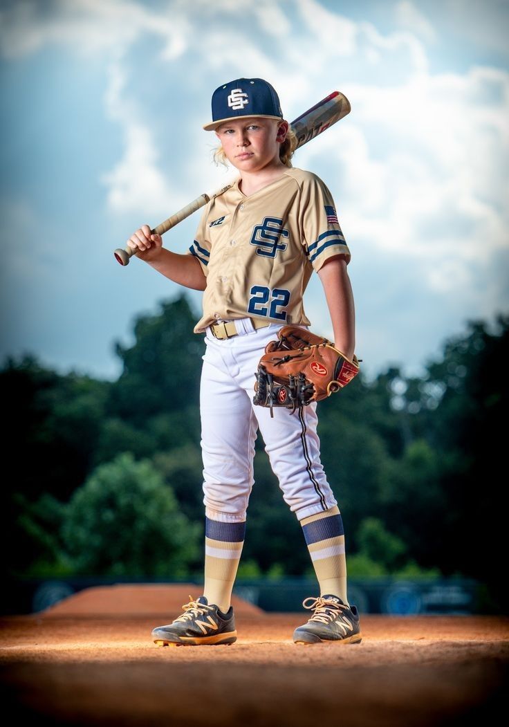 a young boy holding a baseball bat on top of a dirt field with trees in the background