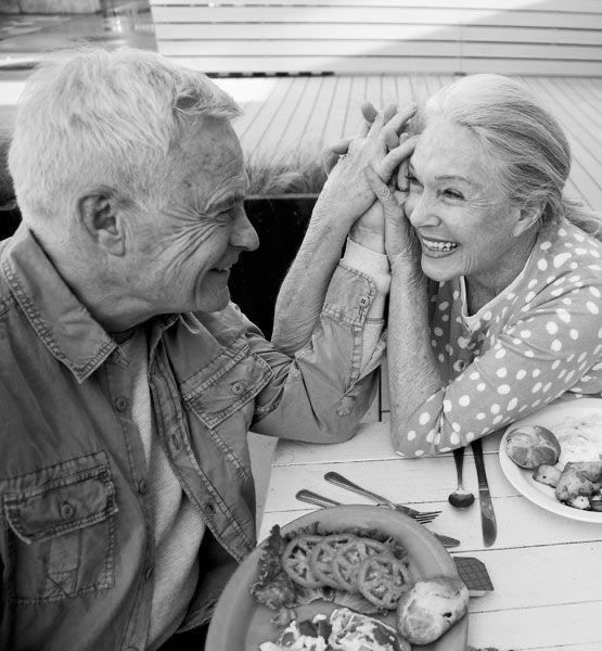 an older man and woman sitting at a table with food