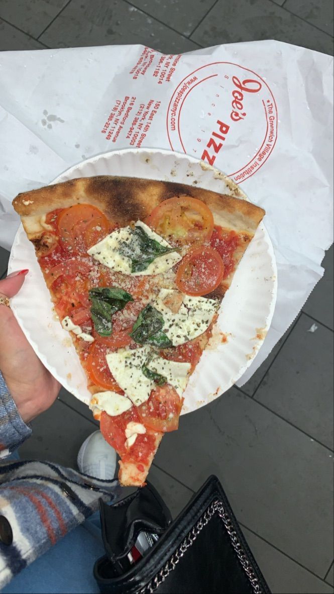 a slice of pizza is being held up by someone's hand with a paper plate