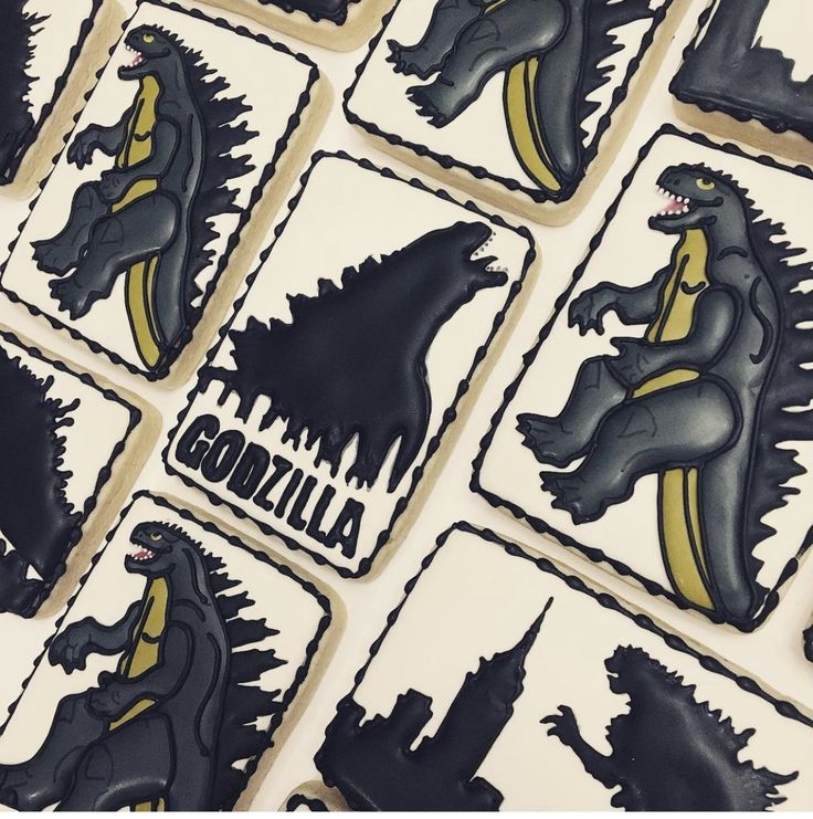 godzilla cookies with black and yellow icing are arranged on a white tablecloth that says godzilla