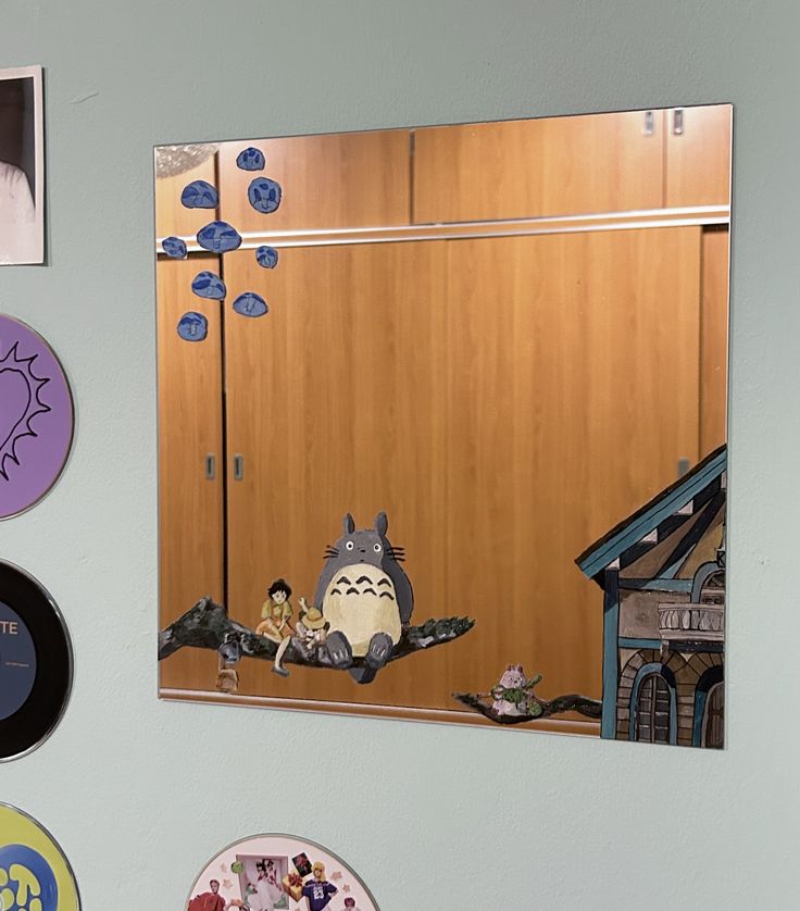 there are many different pictures on the wall above the mirror and in front of it is an image of totoro