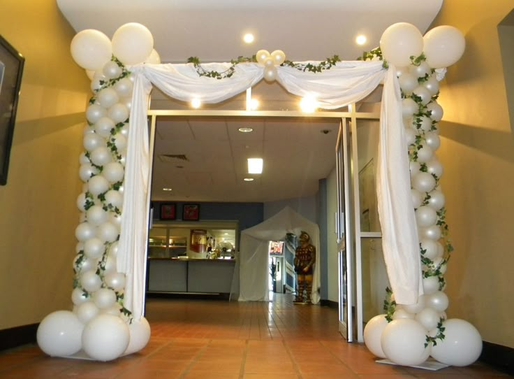 an arch decorated with white balloons and flowers