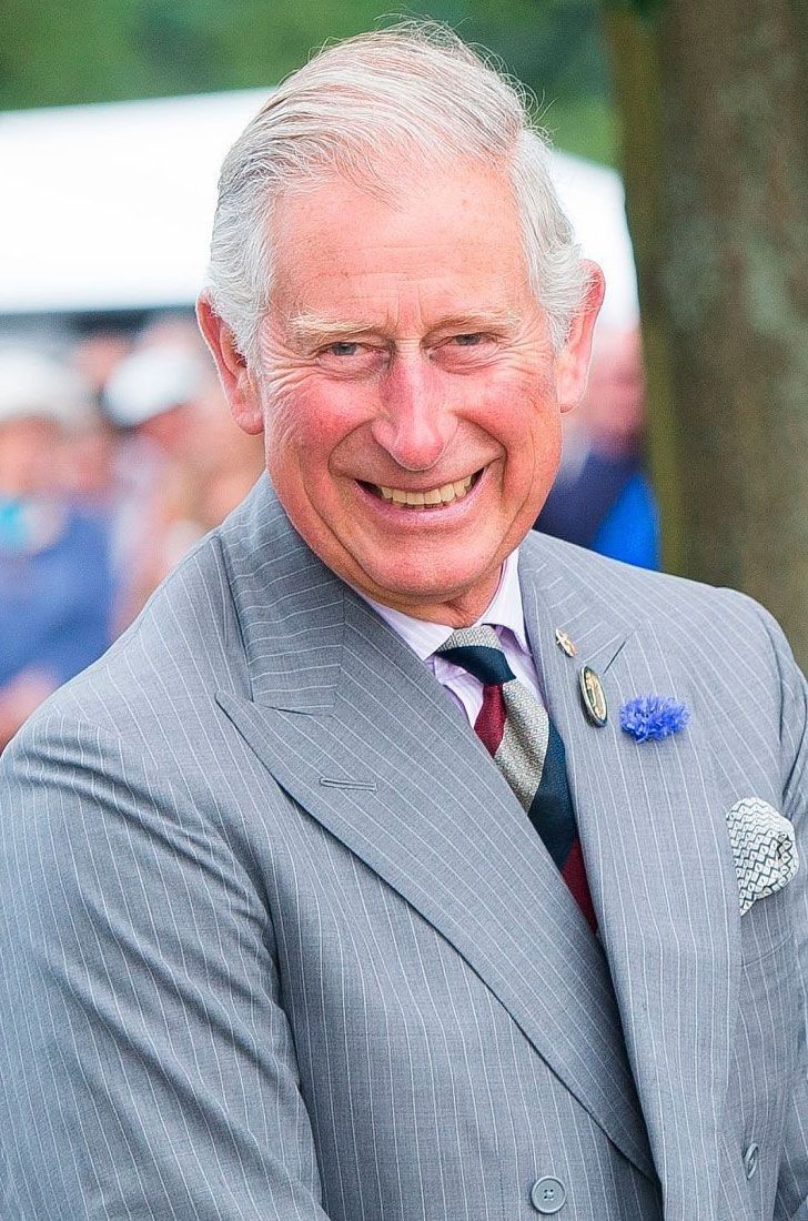 an older man in a suit and tie smiles at the camera while standing next to a tree