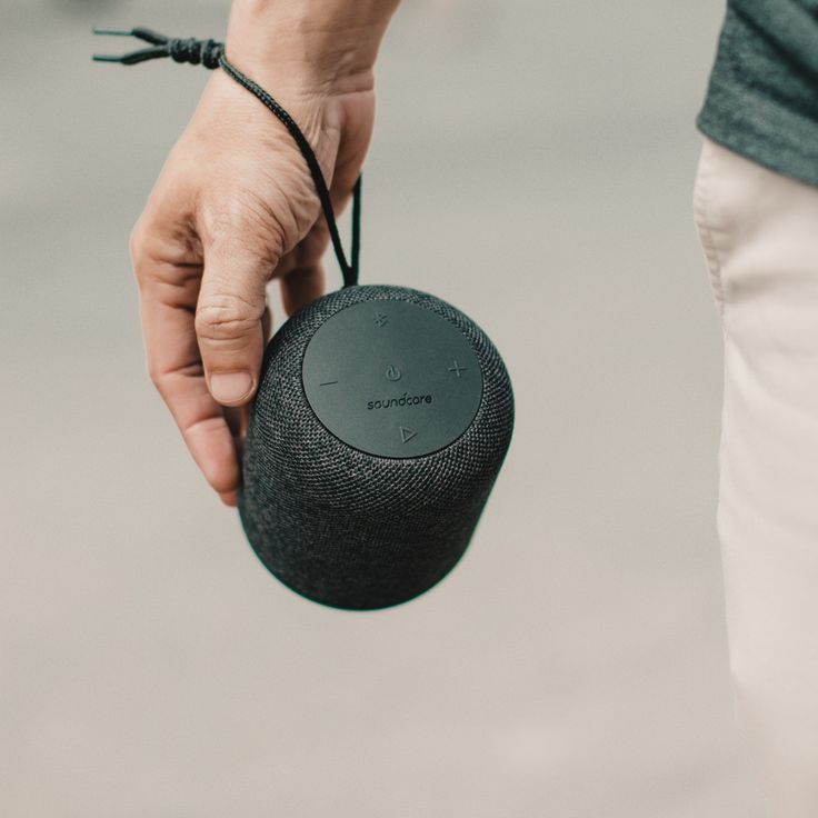 a person holding a black speaker in their left hand and string attached to the device