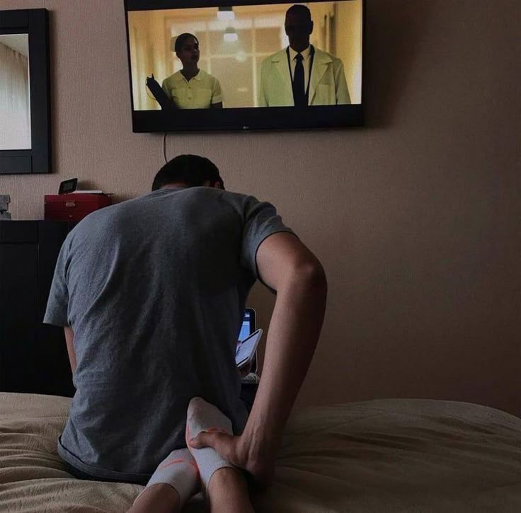 a man sitting on top of a bed in front of a flat screen tv mounted to the wall