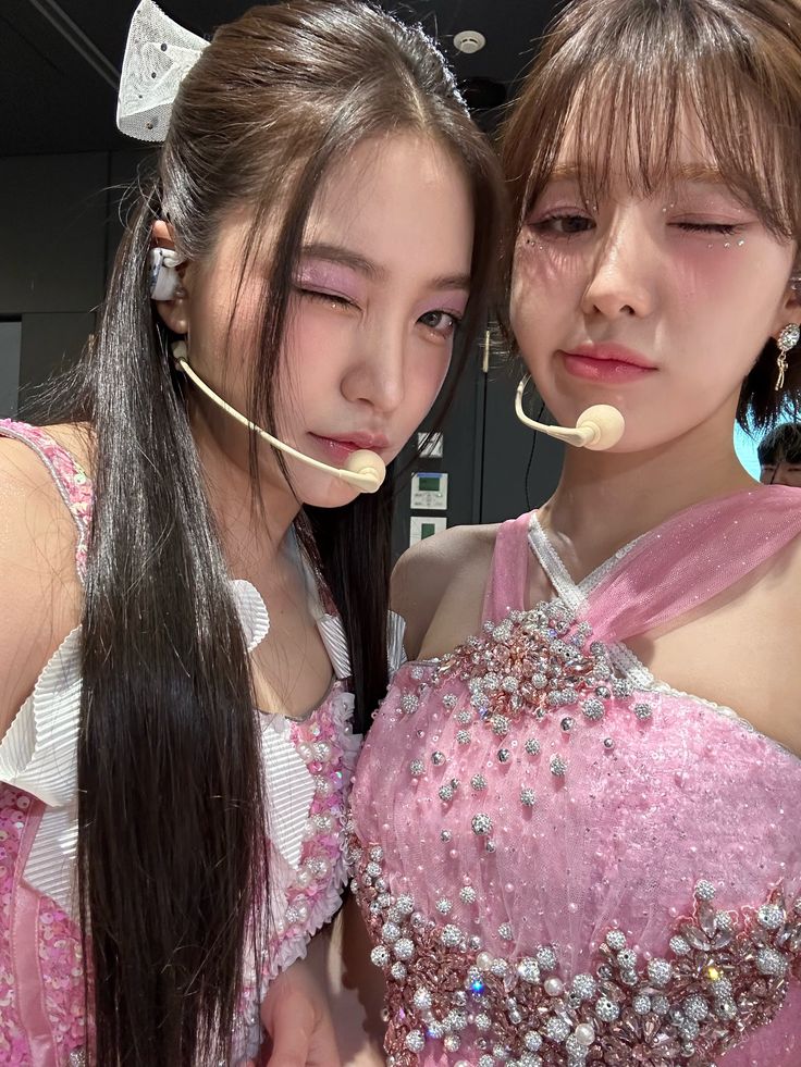 two young women in pink dresses are posing for the camera with their heads covered by ear buds