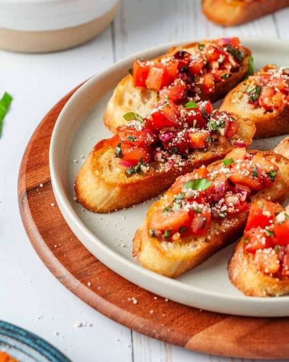 several pieces of bread with tomatoes and parmesan cheese on top sitting on a white plate