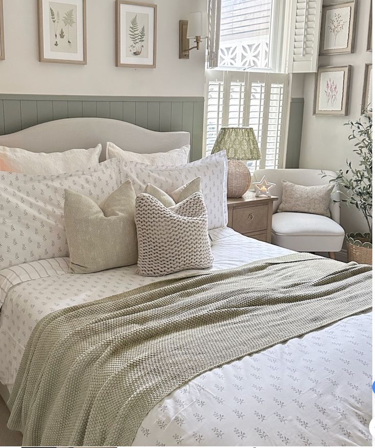 a bed with white and green comforters in a bedroom next to a window filled with framed pictures