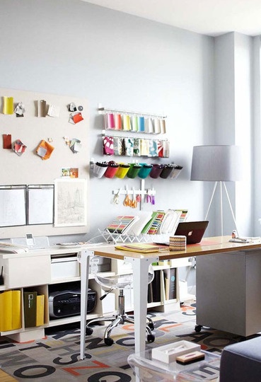 a room with a desk, chair and shelves filled with crafting supplies on the wall