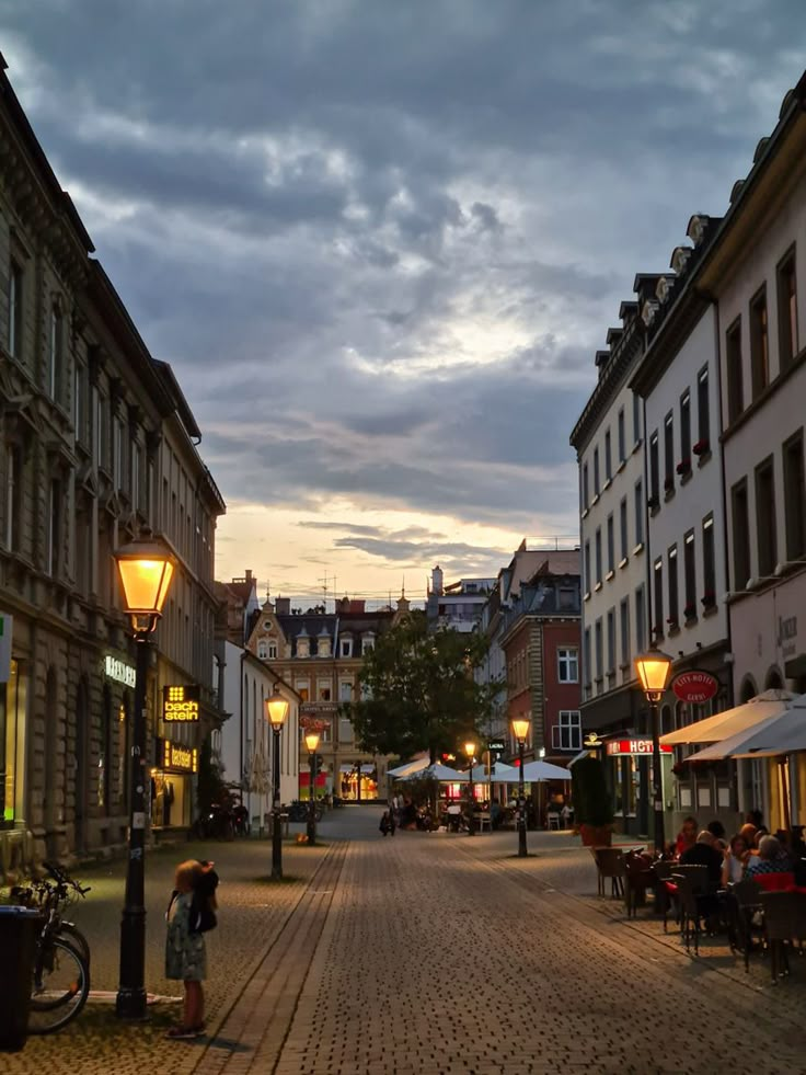 a cobblestone street with people sitting at tables and umbrellas on either side