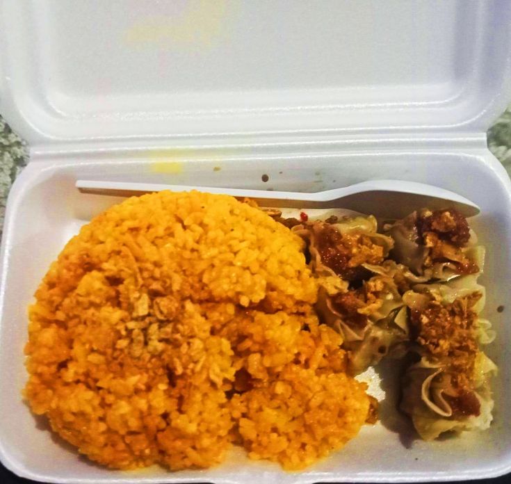 a take out container filled with rice, meat and veggies next to a fork