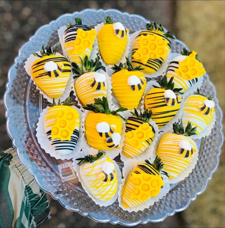 there are many yellow and black decorated strawberries on the platter with green leaves