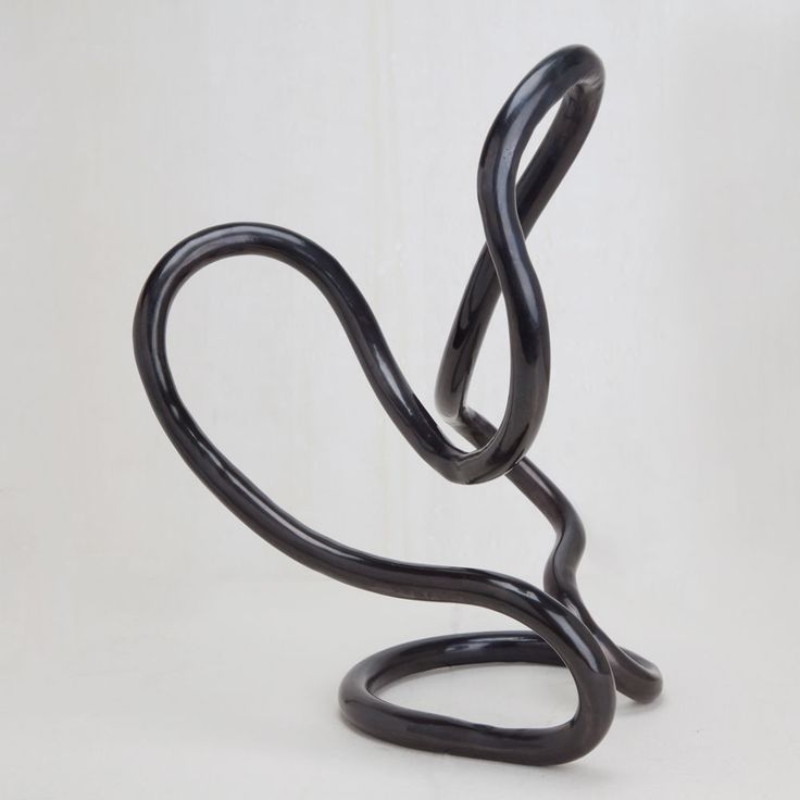 a black sculpture is sitting on a white surface and it looks like a twisted object