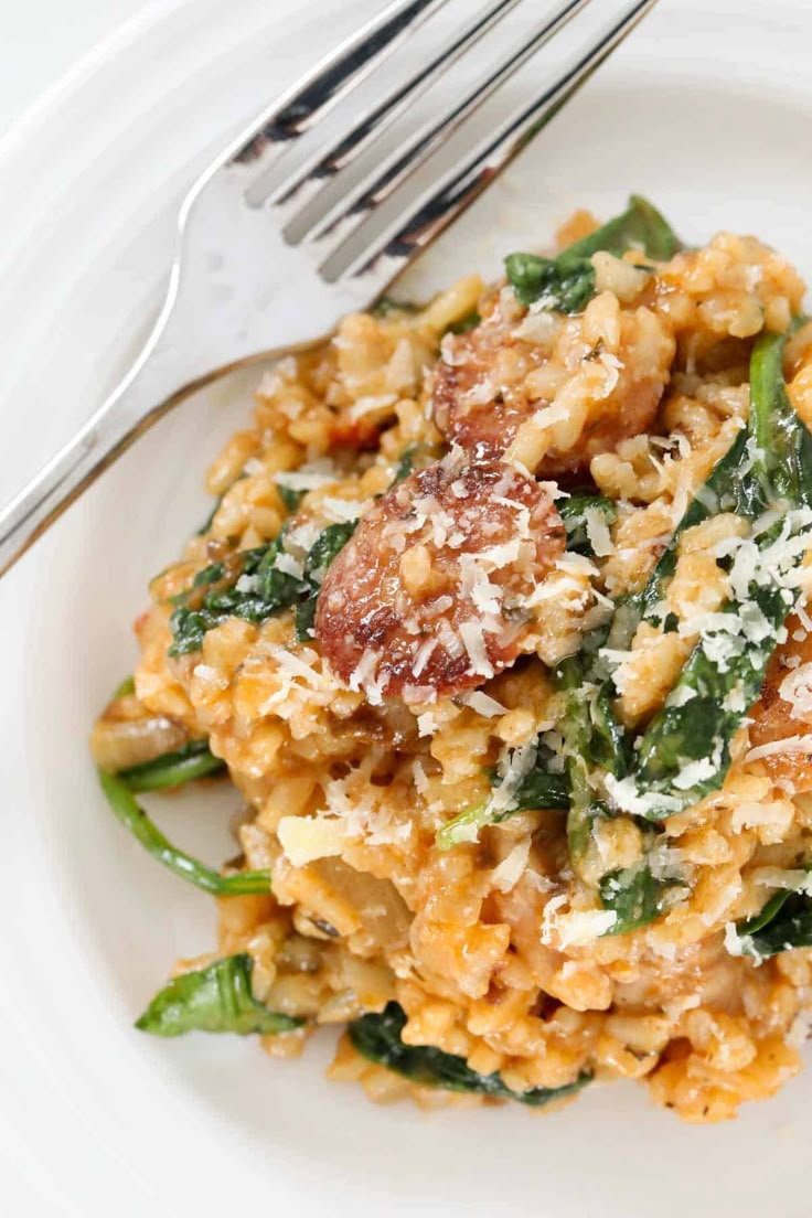 a white plate topped with pasta covered in cheese and spinach next to a fork