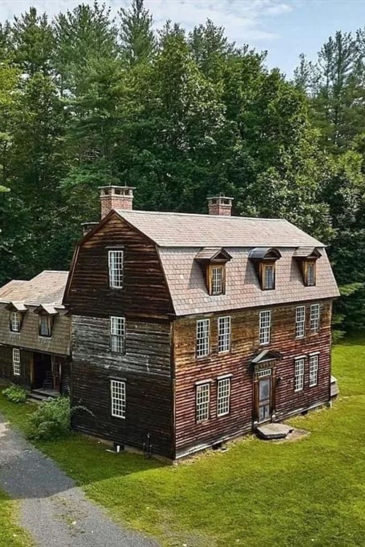 an old wooden house in the middle of a lush green field with lots of trees