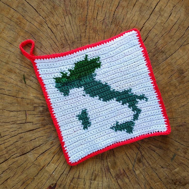 a small crocheted pot holder on top of a wooden table with a red handle