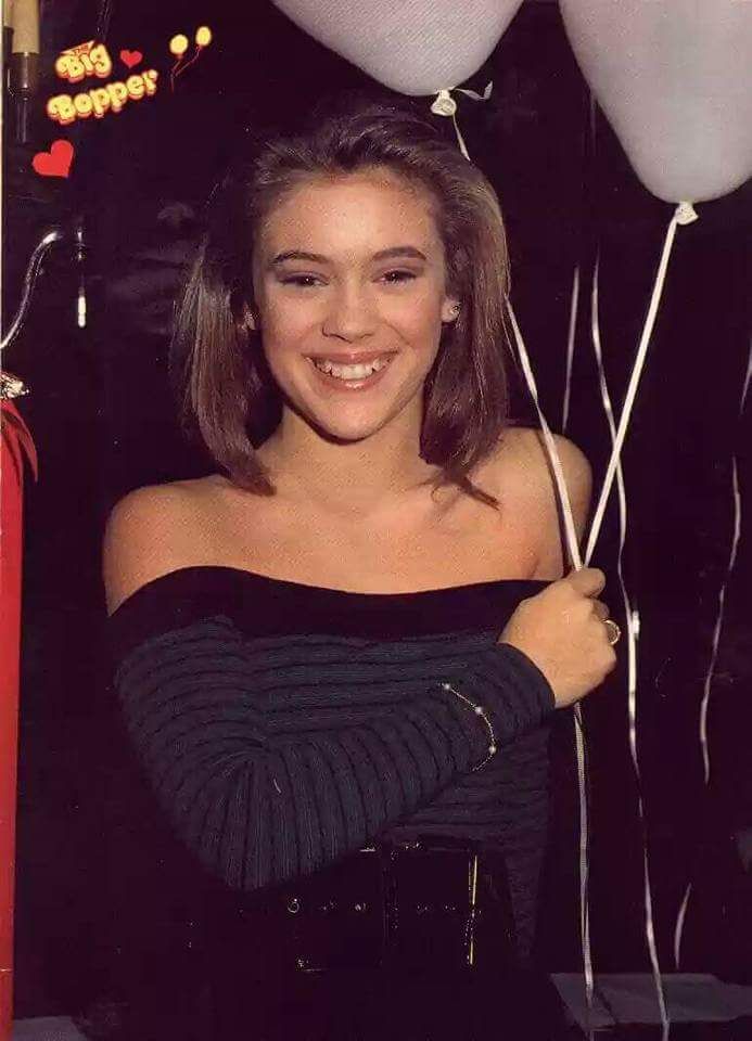 a young woman holding balloons in her hand and smiling at the camera while wearing a black off shoulder top