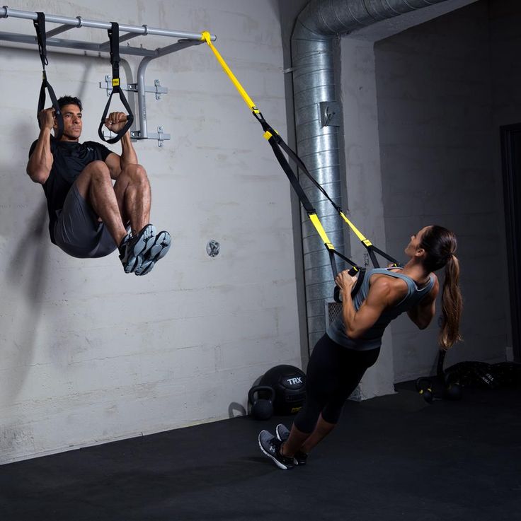 a man and woman doing aerial exercises in a crossfit gym, one holding the bar