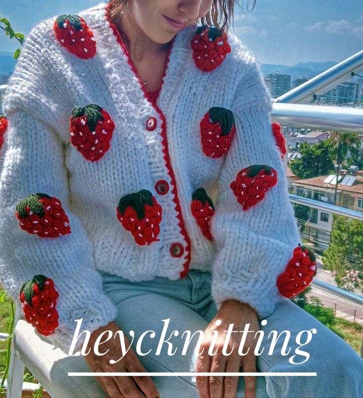 a woman sitting on top of a chair wearing a white sweater with strawberries on it