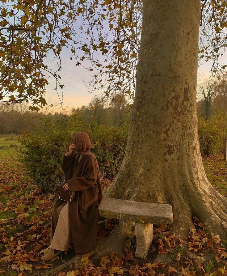 a woman sitting on a bench next to a tree