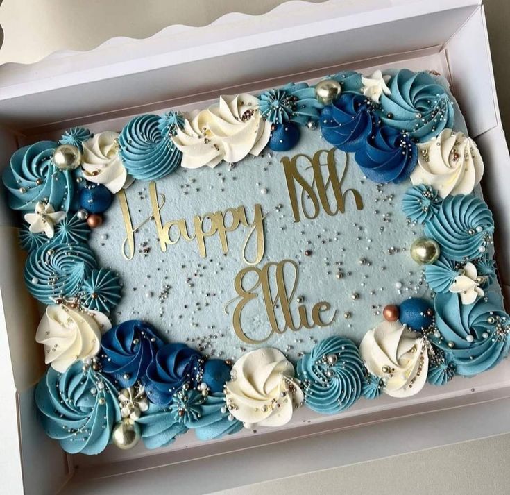 a birthday cake in a box with blue frosting and white flowers on the side