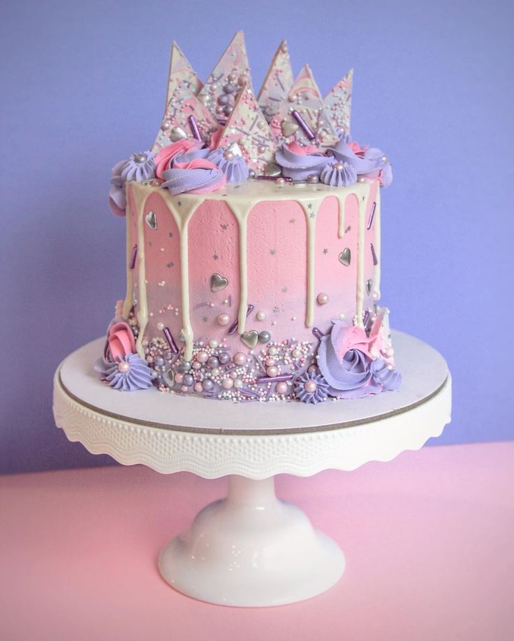 a pink and white cake with purple icing on top sitting on a pedestal in front of a blue wall