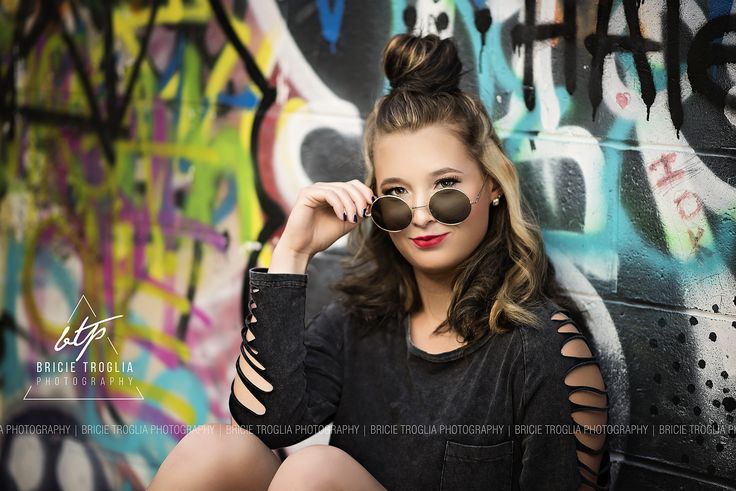 a young woman wearing sunglasses sitting in front of graffiti covered wall