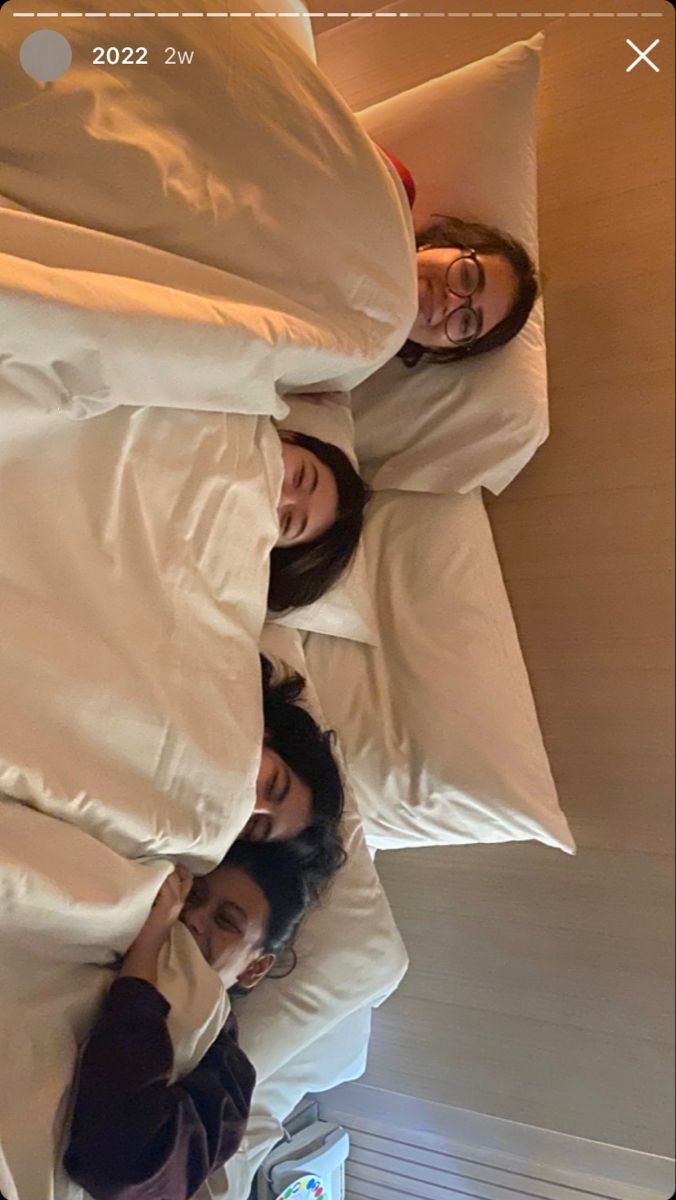 three people laying in bed under covers and pillows